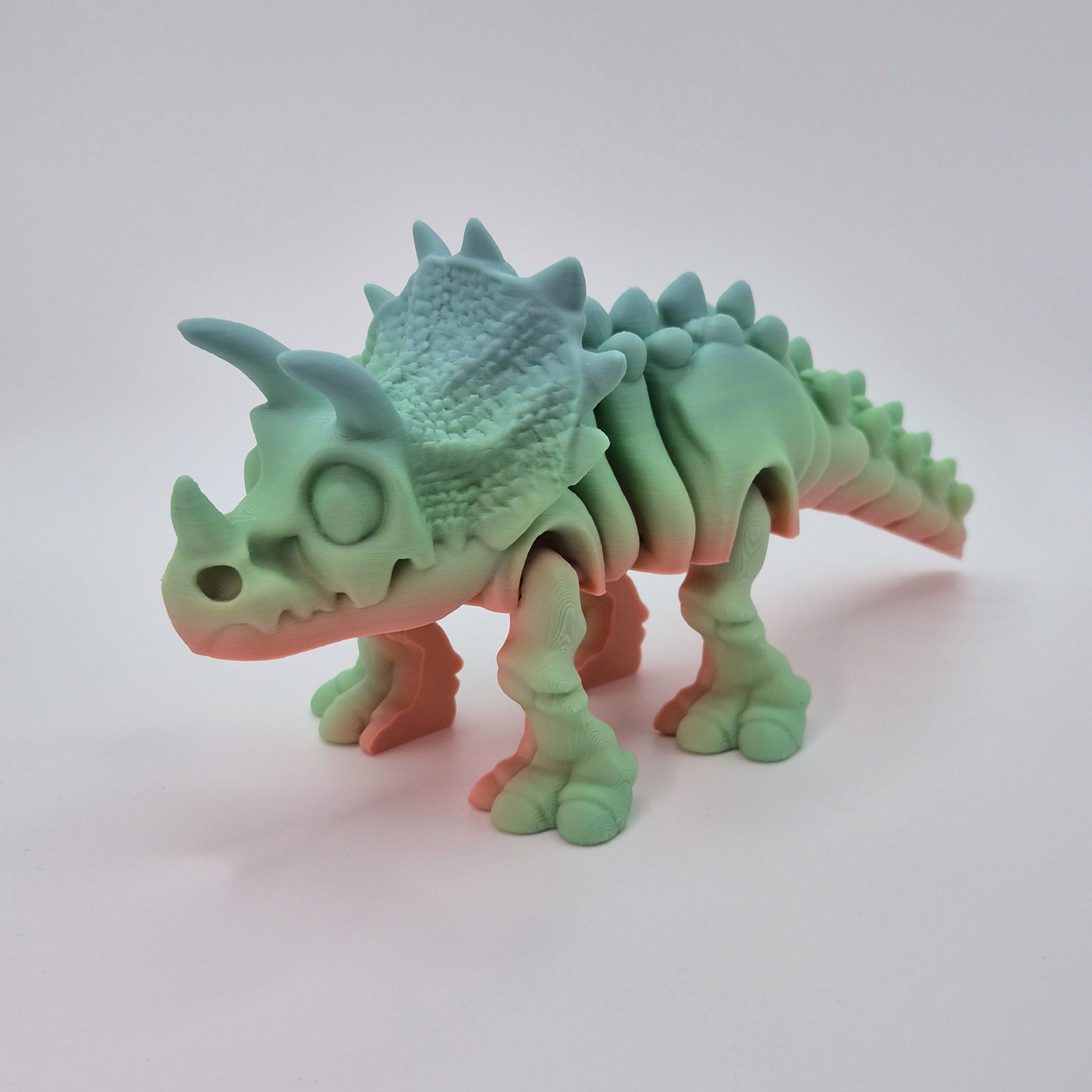 Angled front view of a sherbet-coloured 3D-printed articulating skeleton Triceratops toy