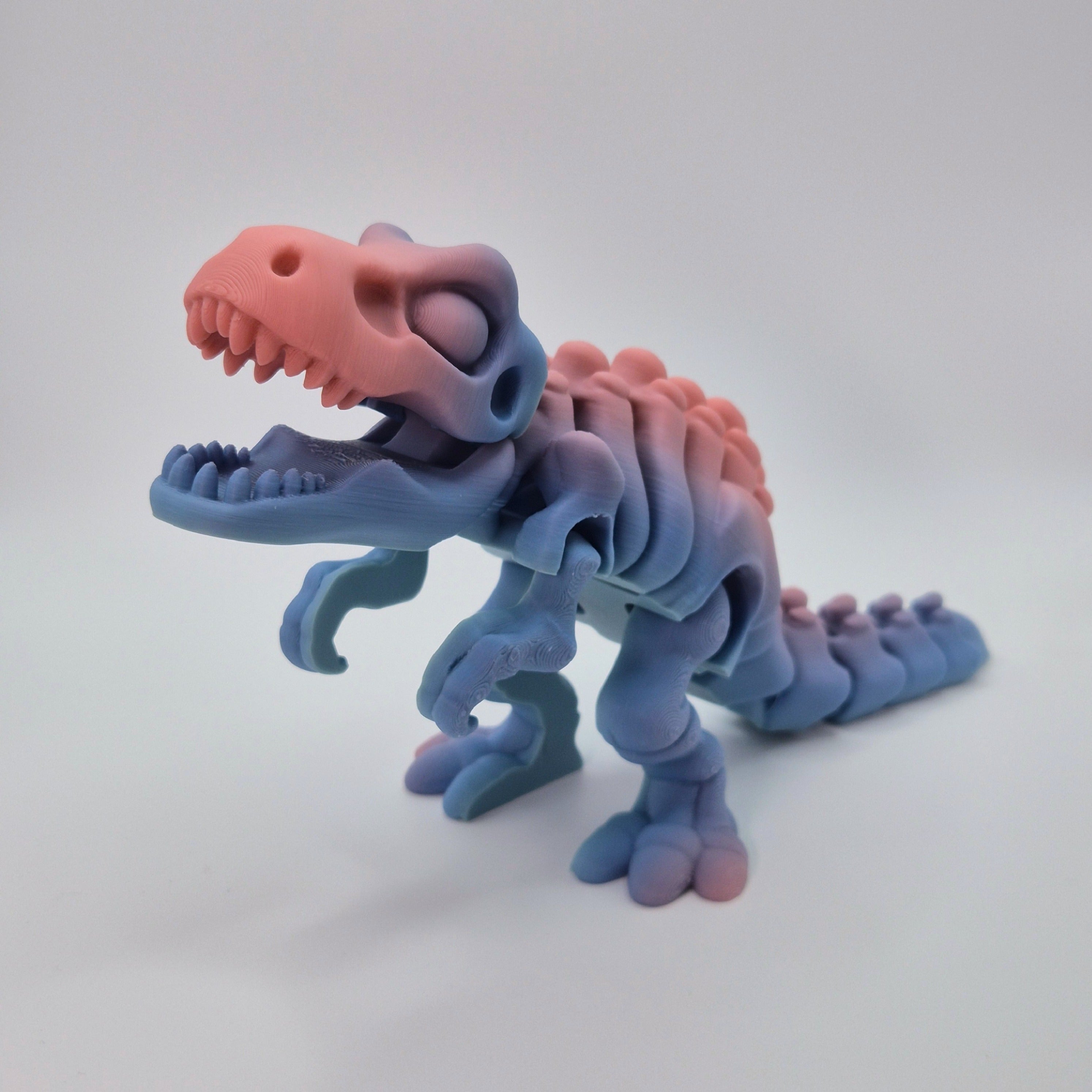 Angled front view of a sherbet-coloured 3D-printed articulating skeleton Tyrannosaurus Rex toy